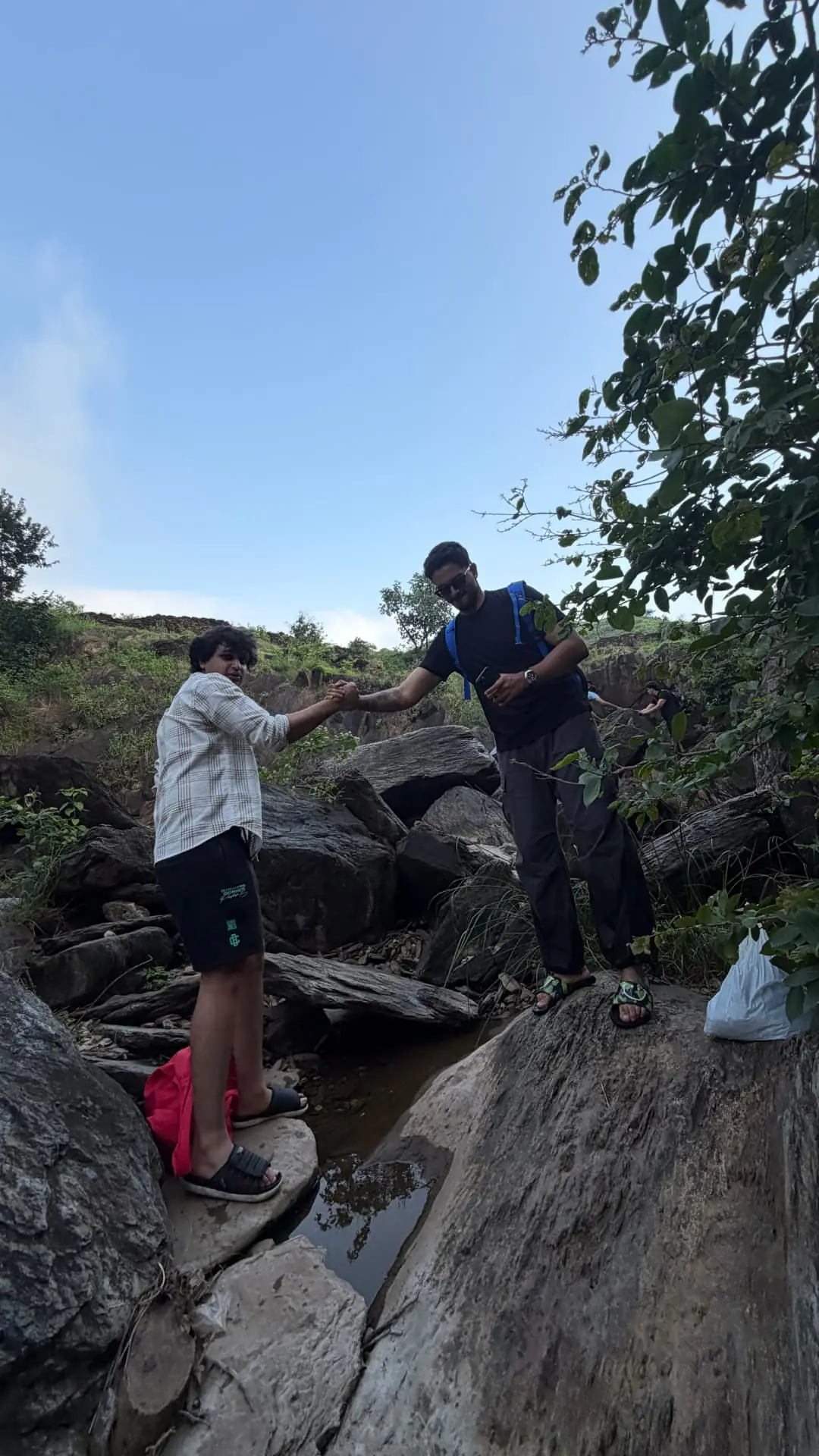 Two travellers helping each other across rocks on the trail